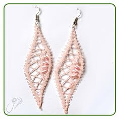 two pairs of pink lace earrings hanging from hooks on a white surface with green border