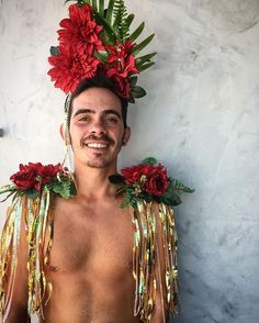 a man with red flowers on his head and gold chains around his neck, standing in front of a white wall