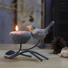 a small bird sitting on top of a metal candle holder with a lit candle in it