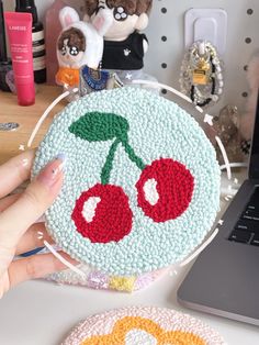 a cake with cherries on it is being held by someone's hand next to a laptop