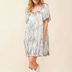 On an ivory background is a model wearing a silver sequin dress with a square neck and puff sleeves. Sequin Dress With Cowboy Boots, Sequin T Shirt Dress, Dresses With Cowboy Boots, Dazzling Dress, Babydoll Mini Dress, Dress Silver, Silver Dress, Sequin Dress, T Shirt Dress