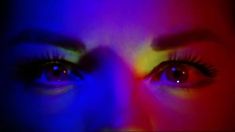 a woman's face with bright colored lights on it and her eyes glowing brightly