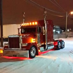 a red semi truck parked on the side of a road in the snow at night