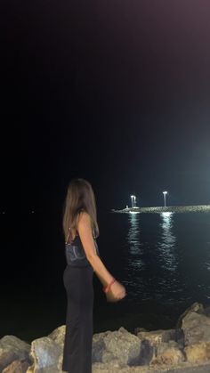 a woman standing on rocks near the ocean at night