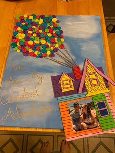 a child's hand holding up a painting with a house and balloons on it