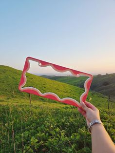 a person holding up a red and white frame in the grass with mountains in the background