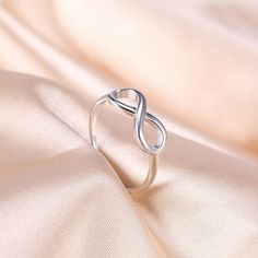 a silver ring sitting on top of a white satin fabric with an infinite knot in the middle