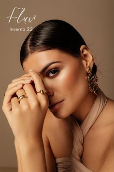 a woman with her hands on her face and wearing gold jewelry, posing for the camera