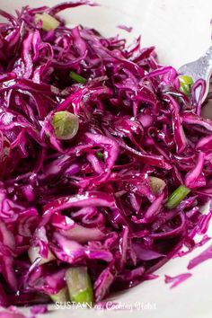 a white bowl filled with red cabbage and green onions next to a silver serving spoon