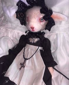 a stuffed animal in a white dress and black bonnet laying on a bed with sheets