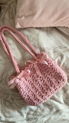 a pink crocheted purse sitting on top of a bed next to a pillow