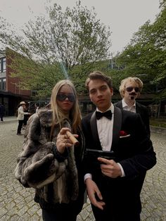 two people dressed in formal wear standing on a cobblestone area with trees and buildings behind them