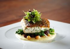 a white plate topped with fish covered in sauce and garnished with green vegetables