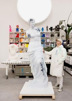 a man standing next to a white statue in a room with shelves and shelving