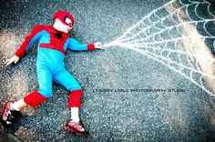 a young boy dressed as spider - man laying on the ground