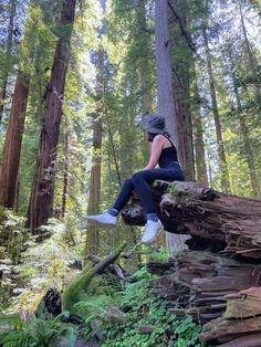 a woman sitting on top of a fallen tree in the middle of a lush green forest