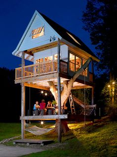 two people standing on the porch of a tree house at night with their lights on