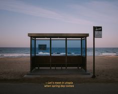 a bus stop sitting on top of a sandy beach next to the ocean at dusk