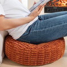 a person sitting on a bean bag chair reading a book in front of a fireplace