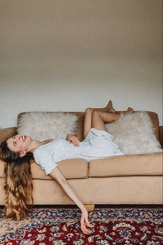 a woman laying on top of a couch in front of a white wall next to a rug