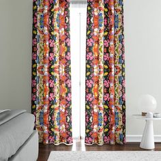 a living room with a couch, chair and window covered in colorful floral curtain panels