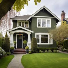 a green house with white trim on the front and side windows, trimmed in grass