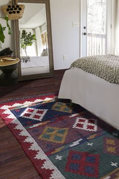 a bed sitting next to a mirror on top of a wooden floor in a bedroom