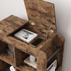 an open wooden table with magazines and a cell phone on it's shelf in front of a white wall