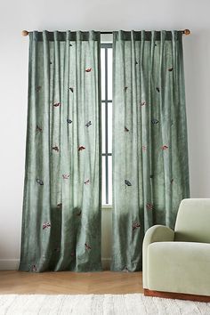 a living room with green curtains and a white chair in front of the window that has birds on it