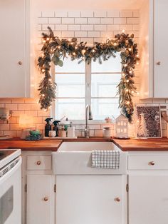 a kitchen decorated for christmas with garland on the window sill and lights hanging over the sink