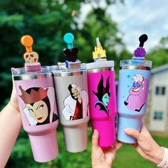 three different colored tumblers with cartoon characters on them in front of some trees and bushes