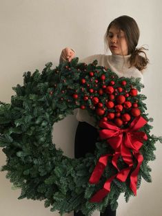 a woman holding a christmas wreath with red berries on it