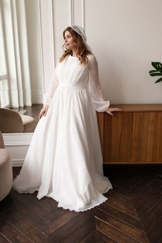 a woman in a white wedding dress standing on a wooden floor next to a window