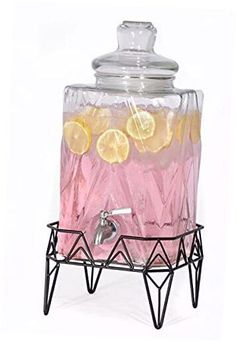 a glass beverage dispenser filled with lemons and pink liquid on a stand