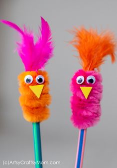 two colorful feathers on top of toothbrushes with googly eyes and beaks