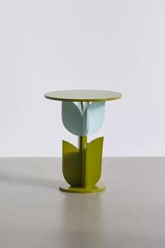 a round table with a green base and two leaves on the top, in front of a white wall