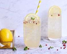 two glasses filled with lemonade and garnish next to some lemons on a table