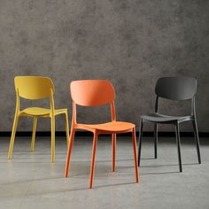 three different colored chairs sitting next to each other in front of a concrete wall and floor