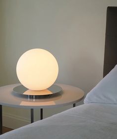 a white ball lamp sitting on top of a table next to a bed in a room