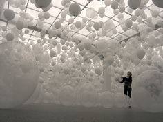 a woman standing in front of a large amount of white balls hanging from the ceiling