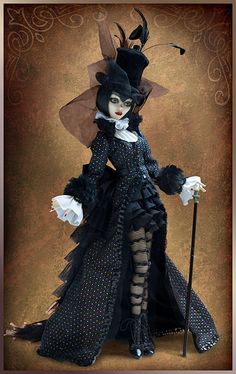 a doll dressed in black and white with a hat, dress and cane standing on a brown background