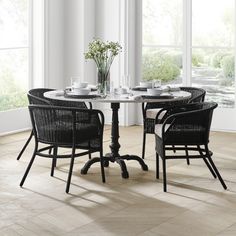 a table with four chairs around it in front of large windows and flowers on the table