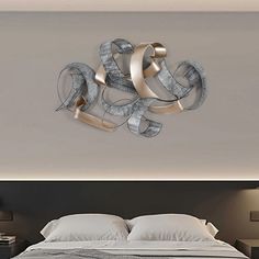 a bed with white sheets and pillows next to a wall mounted art piece on the wall