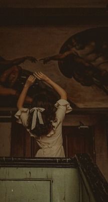 a woman standing on top of a staircase in front of a wall with paintings above her