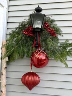 a christmas decoration hanging on the side of a house with red ornaments and greenery