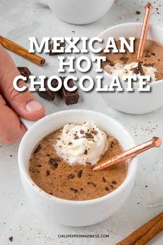 two bowls of mexican hot chocolate with whipped cream and cinnamon sticks on the side, in front of them