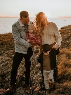 a man and woman holding a baby while standing on top of a hill next to the ocean