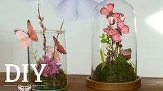 two glass vases with flowers and butterflies in them sitting on a wooden table next to each other