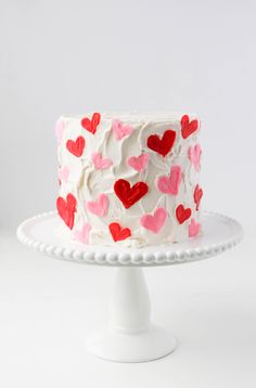 a white cake with red and pink hearts on it, sitting on a plate in front of a white background