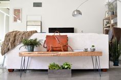 a white couch with a brown bag on top of it and some plants in the corner